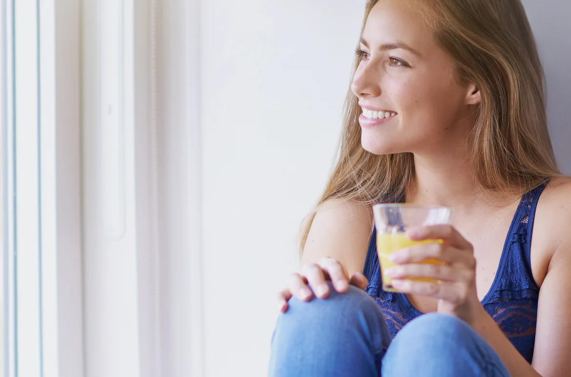 A woman resting by a bright window with a glass of water